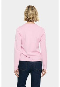 Rosa långärmad tröja med rund halsringning, med en jämn textur. Bärs med mörka denimjeans som har en figursydd design.