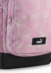 Ružový batoh s bielymi kvetinovými obrysmi, čiernym dnom, sieťovanou bočnou kapsou a logom Puma na čiernej obdĺžnikovej nášivke.