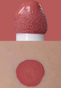Vloeibare lippenstift met een zachte applicatortip, in een gedempte rozenkleur. Veeg op de huid toont een gladde, gelijkmatige laag van dezelfde tint.