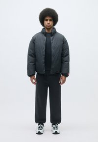 Black puffer jacket with snap buttons, worn over a black sweatshirt. Paired with matching black pants and white athletic shoes.