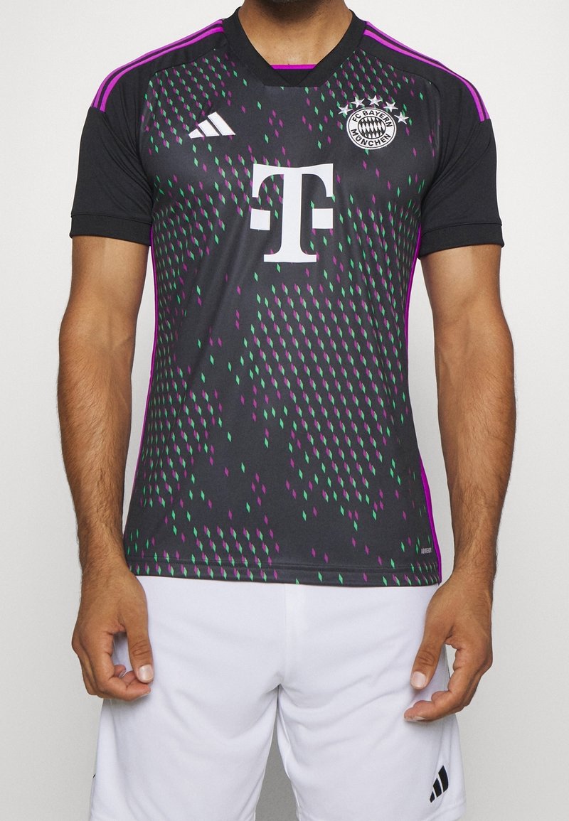 Homme portant un maillot de football noir du FC Bayern Munich avec un motif violet et vert, un logo sponsor blanc et un short blanc.