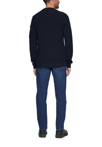 Marineblauwe sweater met textuur en raglanmouwen, gecombineerd met blauwe denim jeans en zwarte schoenen, gezien vanuit de achterkant.