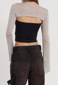 Top croppato nero aderente con maniche lunghe in rete grigia, caratterizzato da una schiena con apertura e abbinato a jeans baggy scuri con tasche a contrasto.