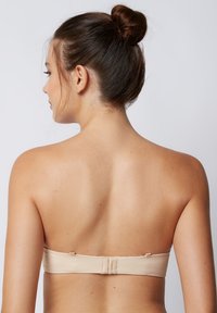 Reggiseno beige senza spalline realizzato in tessuto liscio, con chiusura a gancio sul retro e un design semplice e lineare.