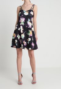 Květinové šaty s vypasovaným korzetem a rozšířenou sukní; mají černou látku s barevnými květinovými vzory, nastavitelné ramínka a hladký povrch.