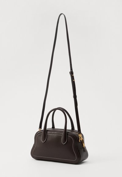 Sac à main en cuir marron avec une forme structurée, deux poignées supérieures, une longue bandoulière réglable et des coutures blanches contrastantes.