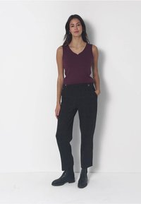 Bordeaux värjetön toppi V-kauluksella, yhdistettynä korkeavyötäröisiin mustiin ruutuhousuihin ja mustiin nilkkureihin. Yksinkertainen muotoilu ilman kuvioita.