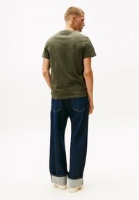 Camiseta de algodón verde oliva con mangas cortas, combinada con pantalones vaqueros de denim azul de pierna ancha con dobladillo vuelto y costuras en contraste.