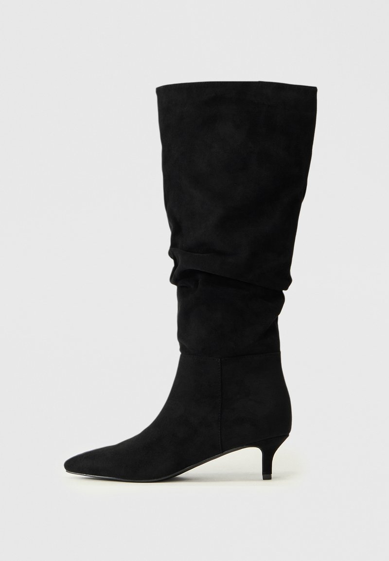Bottes noires en daim à hauteur de genou avec un design fléchissant ; pointe effilée et un petit talon empilé. Texture lisse, sans matériel ou motifs visibles.