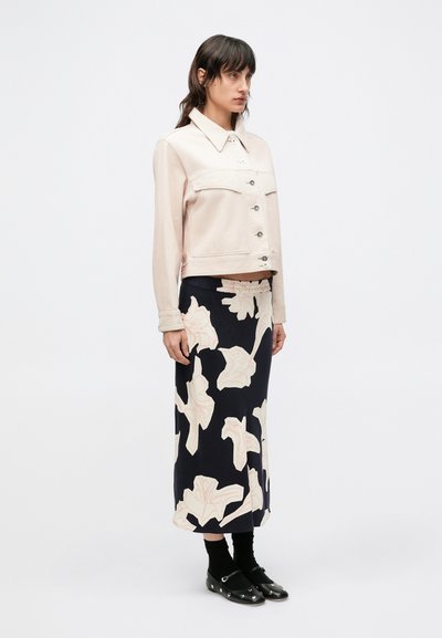 Ανοιχτό ροζ cropped τζιν μπουφάν με κλείσιμο μ ε κουμπιά, συνδυασμένο με μακριά ναυτικό φούστα με μεγάλα floral μοτίβα σε απαλό ροζ. Μαύρα παπούτσια ολοκληρώνουν το ντύσιμο.