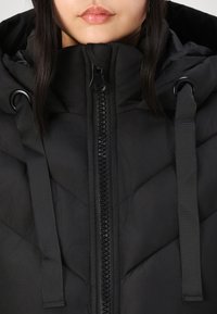 Veste doudoune noire avec fermeture éclair à l'avant, straps ajustables et col haut avec un motif matelassé, fabriquée en tissu doux et texturé.