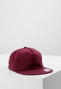Burgundy színű baseball sapka lapos karimával, sima anyagból készült; a tetején egy gomb, az oldalon pedig egy címke található.