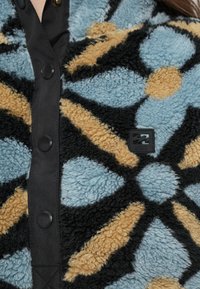 Χνουδωτό, πολύχρωμο φλις μπουφάν με λουλουδάτο μοτίβο σε αποχρώσεις μπλε, μπεζ και μαύρο, με μαύρα κουμπιά πατιλέτας και ταμπελάκι με λογότυπο.