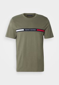 Olivově zelené tričko s krátkým rukávem, s horizontálními pruhy v námořnické modré, bílé a červené barvě a textem "Tommy Hilfiger" přes hruď.