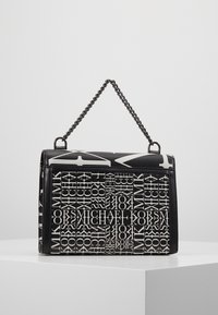 Borsa rettangolare in bianco e nero con manico a catena, caratterizzata da un motivo ripetuto con il testo "Michael Kors" su un piedistallo bianco.