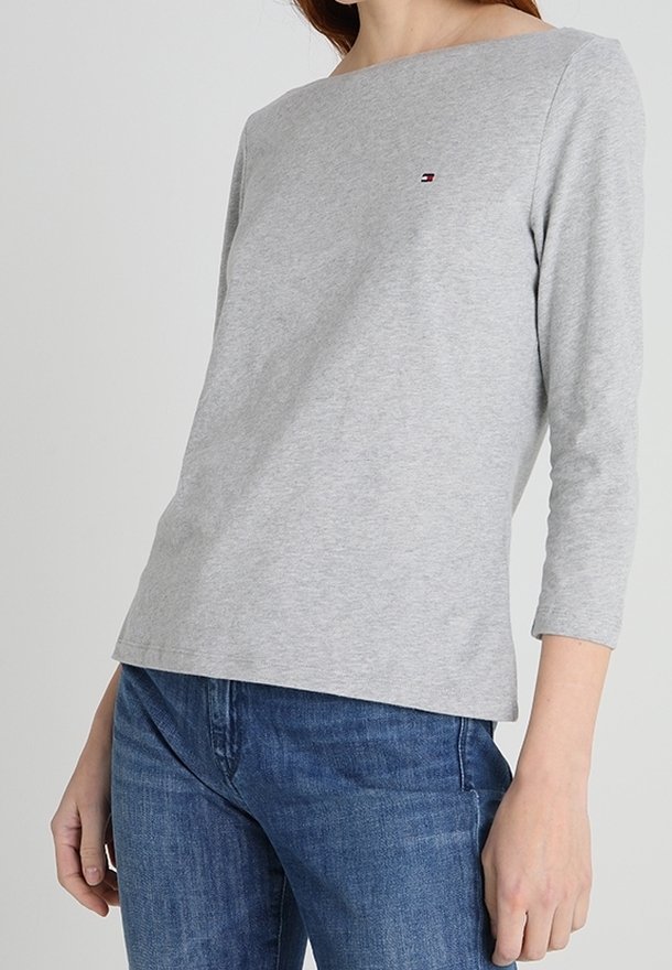 Gray long-sleeve shirt with a wide neckline and a small logo on the chest, made of soft cotton fabric, worn with blue jeans.