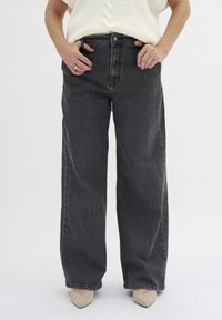 Kalhoty s vysokým pasem a širokými nohavicemi z tmavě šedého denimu, s klasickým zapínáním na knoflík a předními kapsami, kombinované s pleteným krémovým topem.