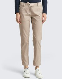 Beige Hose mit Kordelzugbund, seitlichen Taschen und schmal zulaufendem Bein, kombiniert mit weißen Sneakers. Glattes Baumwollmaterial.