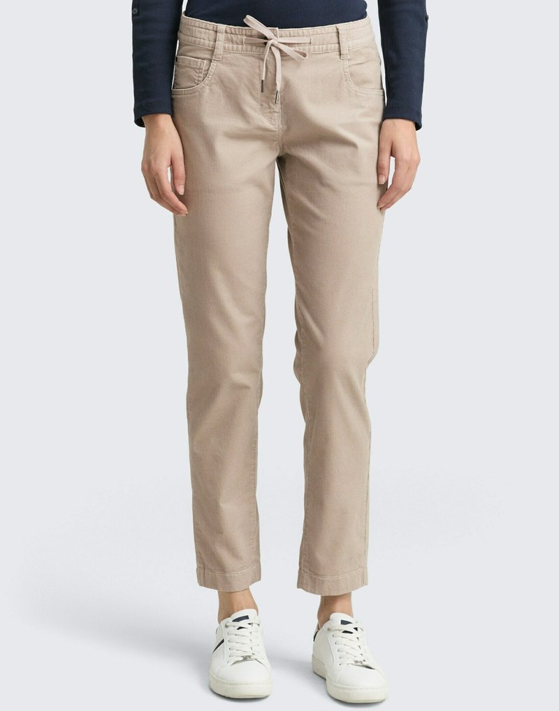 Beige Hose mit Kordelzugbund, seitlichen Taschen und schmal zulaufendem Bein, kombiniert mit weißen Sneakers. Glattes Baumwollmaterial.