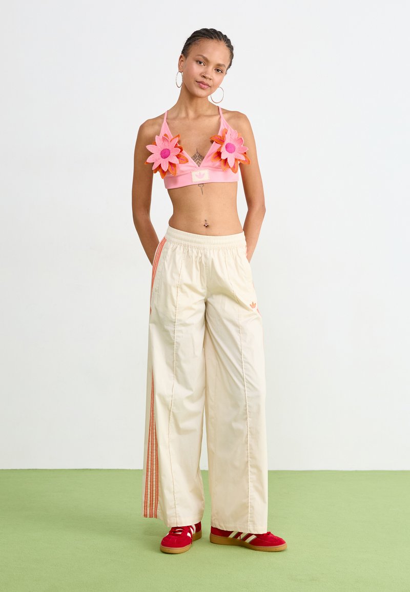 Różowy top w stylu crop z kwiatowymi akcentami, kremowe spodnie szerokie z pomarańczowymi paskami i czerwone sneakersy z białymi paskami, prezentowane na modelce.