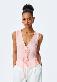 Rosa ärmelloses Oberteil mit tiefem V-Ausschnitt und Schnürdetails an der Vorderseite. Hergestellt aus leichtem Stoff, zeichnet es sich durch ein tailliertes Design und eine weiche Textur aus.