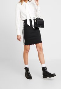 Svart stickad kjol med vita ränder, parat med en vit blus med slipskrage. Svarta ankelstövlar med bred sula fulländar looken.