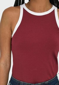 Top de tirantes burdeos con textura acanalada y ribete blanco en el cuello y las sisas. Textura suave con un diseño ajustado, combinado con pantalones cortos de mezclilla azules.