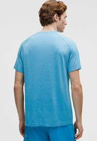 Jasnoniebieska koszulka sportowa z krótkim rękawem. Wykonana z teksturowanej tkaniny, z delikatnym wzorem na powierzchni i okrągłym dekoltem.