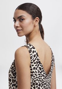 Mouwloze top met luipaardprint, gemaakt van gladde stof. Heeft een diepe V-rug en schouderbanden in zwart en beige kleurenschema.