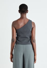 Top grigio asimmetrico con design a spalla unica, corpetto aderente e texture liscia, abbinato a pantaloni larghi grigi.
