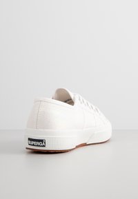 Baskets blanches avec une texture irisée, bout arrondi et design à lacets. Comprend une semelle en caoutchouc et un logo de la marque au talon.