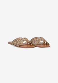 Sandali piatti con suola in pelle beige, decorati con cinturini metallici dorati intrecciati che presentano un motivo texturizzato.