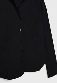 Sort skjorte med knapper, lavet af glat stof, med klassisk krave, lange ærmer og en buet kant med flere sorte knapper.