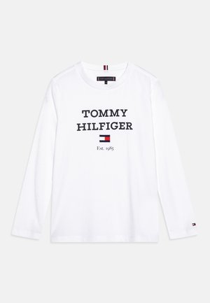 Weißes Langarmshirt mit „TOMMY HILFIGER“-Text, dem Flaggenlogo der Marke und „Est. 1985“ auf der Vorderseite in der Mitte gedruckt.