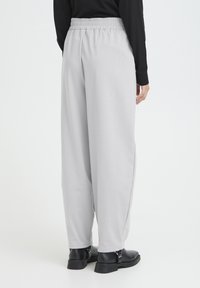 Pantalon gris clair, ample, avec une ceinture élastique. Présente une texture lisse et une coupe large, associé à des bottines noires.