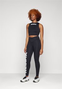 Crop top sport negru cu logo-ul "NEBBIA", asortat cu colanți negri cu talie înaltă, care prezintă imprimeul alb "NEBBIA" și un material texturat.