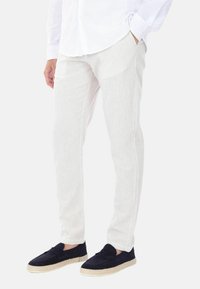 Pantaloni leggeri in crema, con texture e strisce verticali, dotati di tasche laterali e vestibilità slim. Abbinati a scarpe stile espadrillas di colore blu navy.