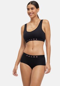 Zwarte sportbeha en high-waisted slip met een subtiele textuur. Beide hebben een roze "FALKE" -logo op de tailleband.
