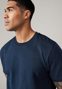 Marineblauwe t-shirt met ronde hals, voorzien van een gestructureerd patroon aan de voorkant, gemaakt van zacht materiaal met korte mouwen en een gladde afwerking.