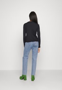 Zwart lange mouwen top, lichtblauwe high-waisted jeans, groene suède platformhakken, gezien vanuit de achterkant. Eenvoudig ontwerp en zachte textuur.