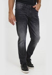 Jeans de mezclilla gris oscuro con un acabado desgastado, diseño de pierna recta, cinco bolsillos y costuras sutiles. Llevados con zapatillas deportivas negras.