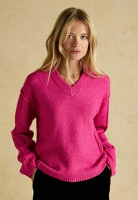 Pulover supradimensionat, cu decolteu în V, de culoare roz aprins, realizat dintr-un material tricotat moale, cu manșete și tiv cu dantelă, având detalii pe cusăturile laterale.