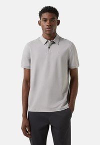 Light gray short-sleeve polo shirt with a classic collar, button placket, and subtle logo detail, made from smooth, breathable fabric.
