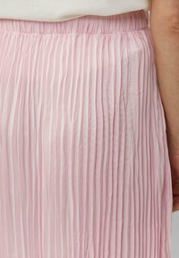 Jupe plissée rose en tissu léger. Présente une surface texturée avec des plis verticaux, et une ceinture élastique pour plus de flexibilité.