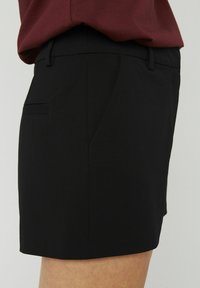 Shorts noirs ajustés au toucher lisse, avec une poche latérale et une taille cintrée. Le design présente une silhouette épurée et simple.