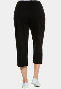 Schwarze kurze Hosen mit einer lockeren Passform und elastischem Bund, mit einer glatten Textur und umgeschlagenen Säumen. Kombiniert mit weißen Sneakers.
