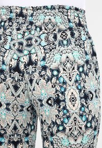 Daudzkrāsaini stiepļu bikses ar elastīgu jostasvietu, kas izrotāta ar ziedu un ģeometrisku rakstu tumši zilos, krēmkrāsas un gaiši zilos toņos.