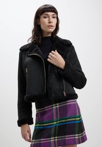 Giacca in finta shearling nera con un ampio colletto e chiusura a zip; presenta una fodera morbida e un design cropped. Abbinate a una gonna a quadri.