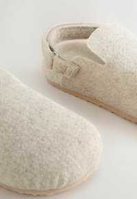 Beige felt slippers with open-back design, soft texture, and light-colored rubber sole. Features a buckle accent for an adjustable fit.