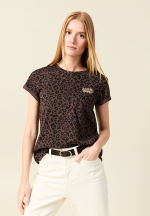 Camiseta de algodón con estampado de leopardo marrón y mangas enrolladas, con texto dorado "dancing queen"; combinada con jeans blancos de tiro alto y cinturón negro.